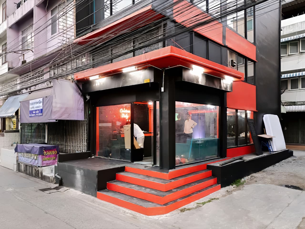 Street view of the Bangkok Podcast Studio building in On Nut, a corner block with a red and black facade and glass frontage.