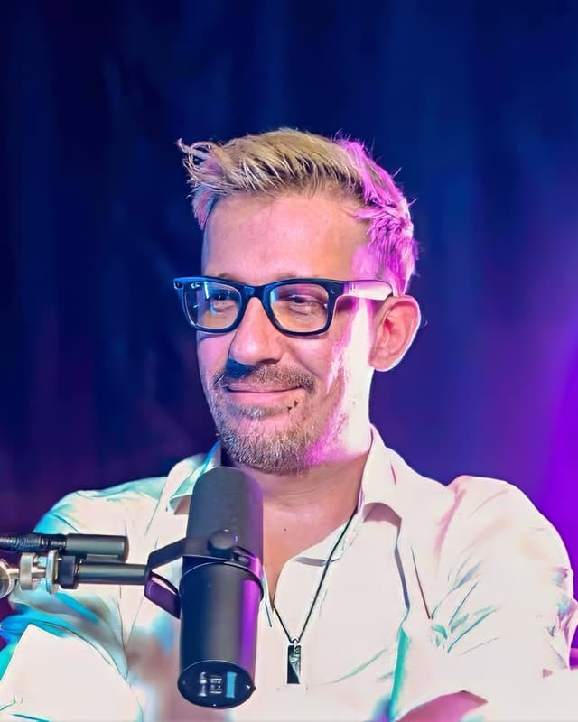 The instructor seated at a microphone in a podcast studio at Bangkok Podcast Studio, under blue and magenta lighting.