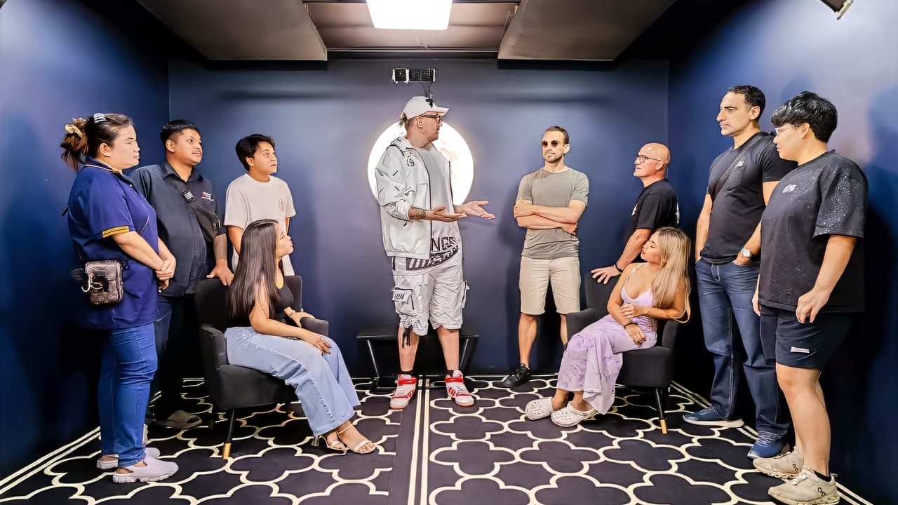 Blue walled room at Bangkok Podcast Studio, about ten people standing and seated in a circle around one person speaking, during a podcast session.